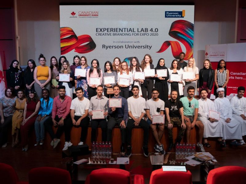 A group of students smiling and posing for a photo on a stage, with some individuals holding certificates.